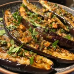 Close-up side view of roasted aubergines showcasing a golden-brown exterior and garnishes.