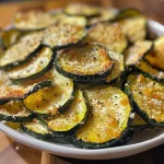 ['Crispy zucchini chips arranged in a circular pattern on a plate.', 'Close-up view of golden-brown baked zucchini chips on a wooden table.', 'A delicious serving of zucchini chips with visible seasoning and texture.', 'Side view of freshly baked zucchini chips with a juicy appearance.']