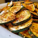 ['Close-up view of crispy zucchini chips with a golden-brown exterior.', 'A side angle of freshly made zucchini chips, lightly seasoned and crunchy.', 'Crispy golden zucchini chips arranged in a bowl, showcasing their texture.', 'Detailed shot of zucchini chips, emphasizing their crispiness and seasoning.']