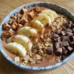Close-up of a chocolate banana smoothie bowl topped with fruits and granola.