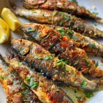 Close-up view of crispy fried sardines garnished with lemon wedges and parsley.