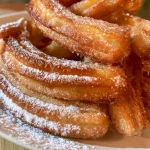 Gros plan de churros croustillants dorés dans une assiette.